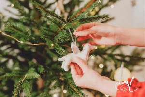 Hands Gently Hang a Ceramic Angel Dog Ornament on a Christmas Tree Honoring the Memory of a Beloved Pet During the Holiday Season